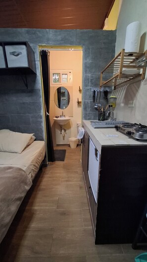 Une petite pièce comprenant un lit, un coin cuisine, un évier et un miroir.