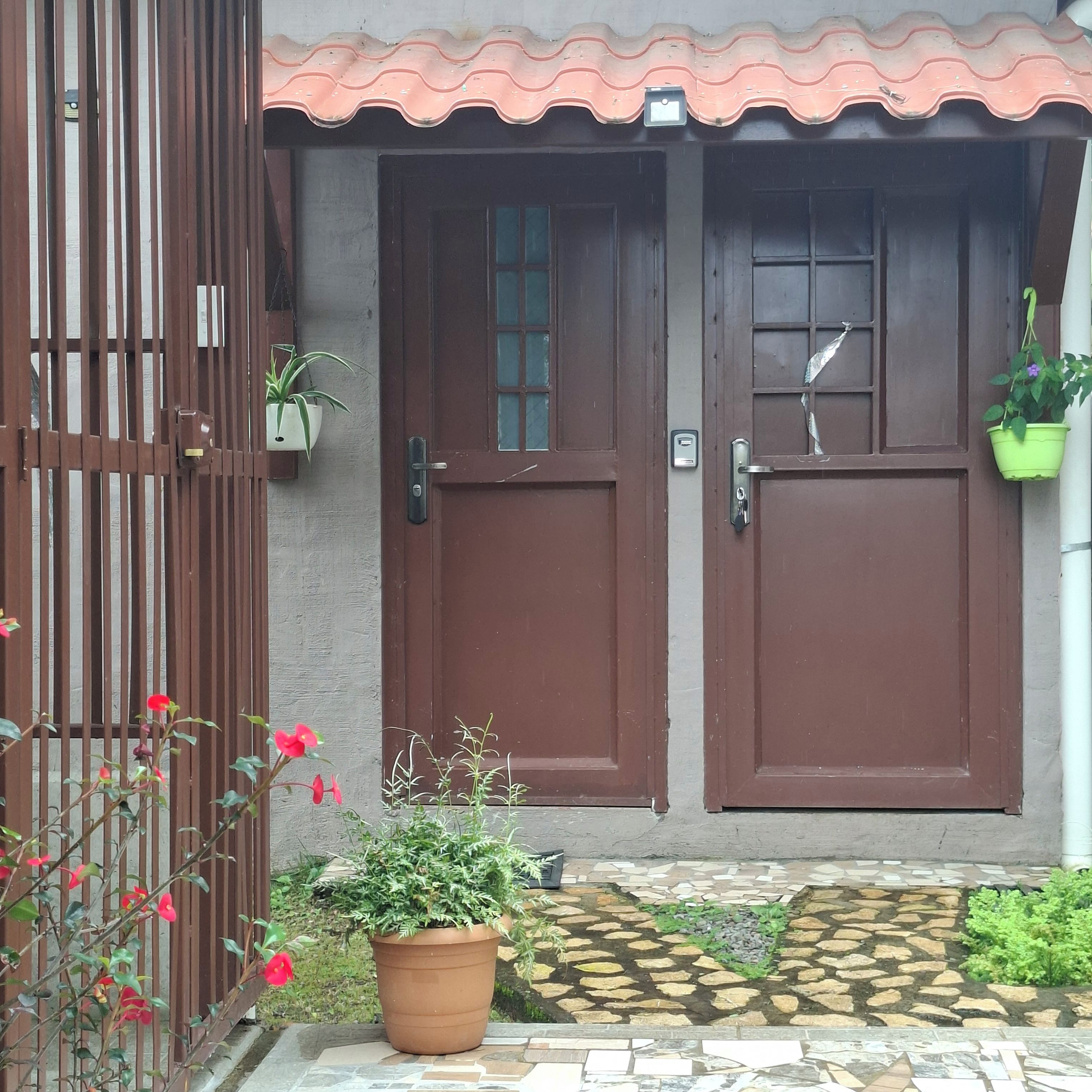 A house with two brown doors, a tiled entrance, and a potted plant in the foreground.