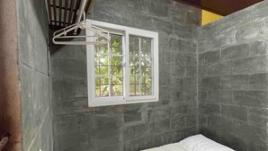 Un baño pequeño y cerrado con una cama individual, una ventana y un perchero para toallas.