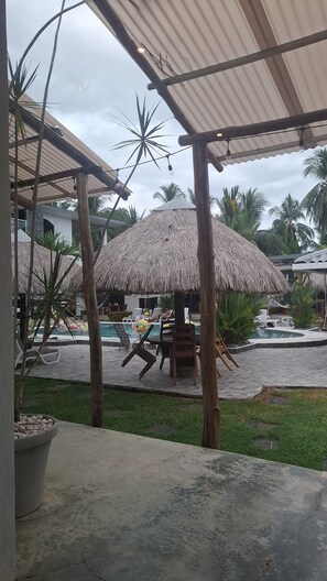 A pool area with thatched umbrellas, lounge chairs, and a view of a building in the background. - Apartamento Single Tiny - Alto Boquete (Alto Boquete)