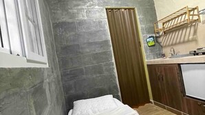 Una habitación pequeña y compacta con pared de ladrillo gris, una puerta de madera y un ventanal pequeño.