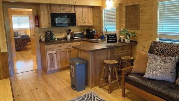A wooden cabin interior with a kitchen, dining area, and a living room. - Asheboro 1BR Cabin Near NC Zoo | Loft & Water View (Asheboro)