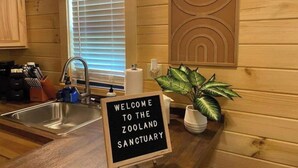 A kitchen with a sink, a window with blinds, a welcome sign, and a potted plant. - Asheboro 1BR Cabin Near NC Zoo | Loft & Water View (Asheboro)