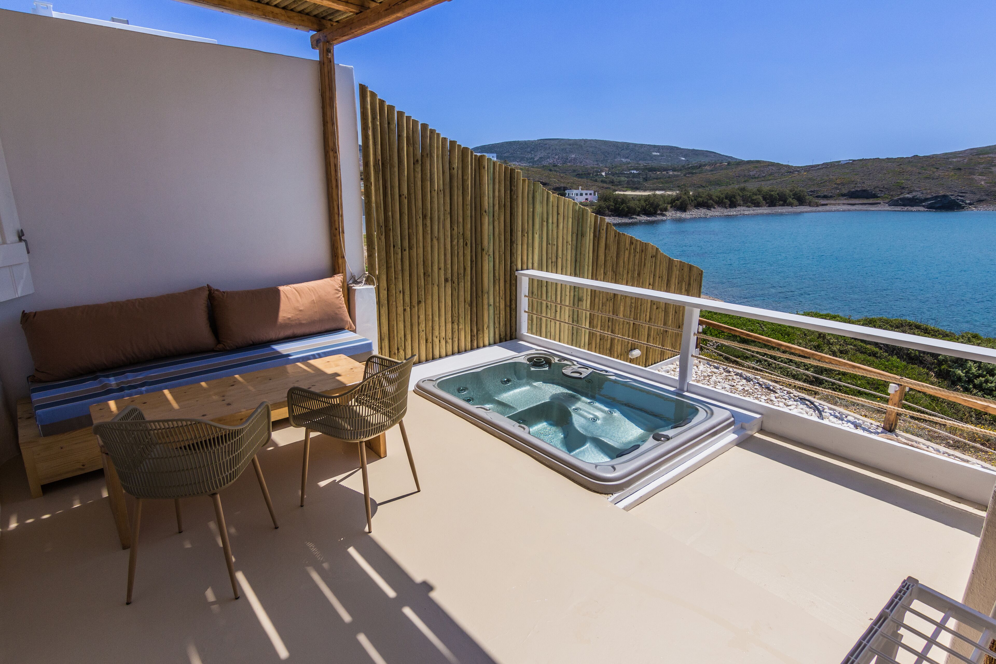 Un balcón con cercado de madera, un jacuzzi, un sofá y dos sillas de mimbre.
