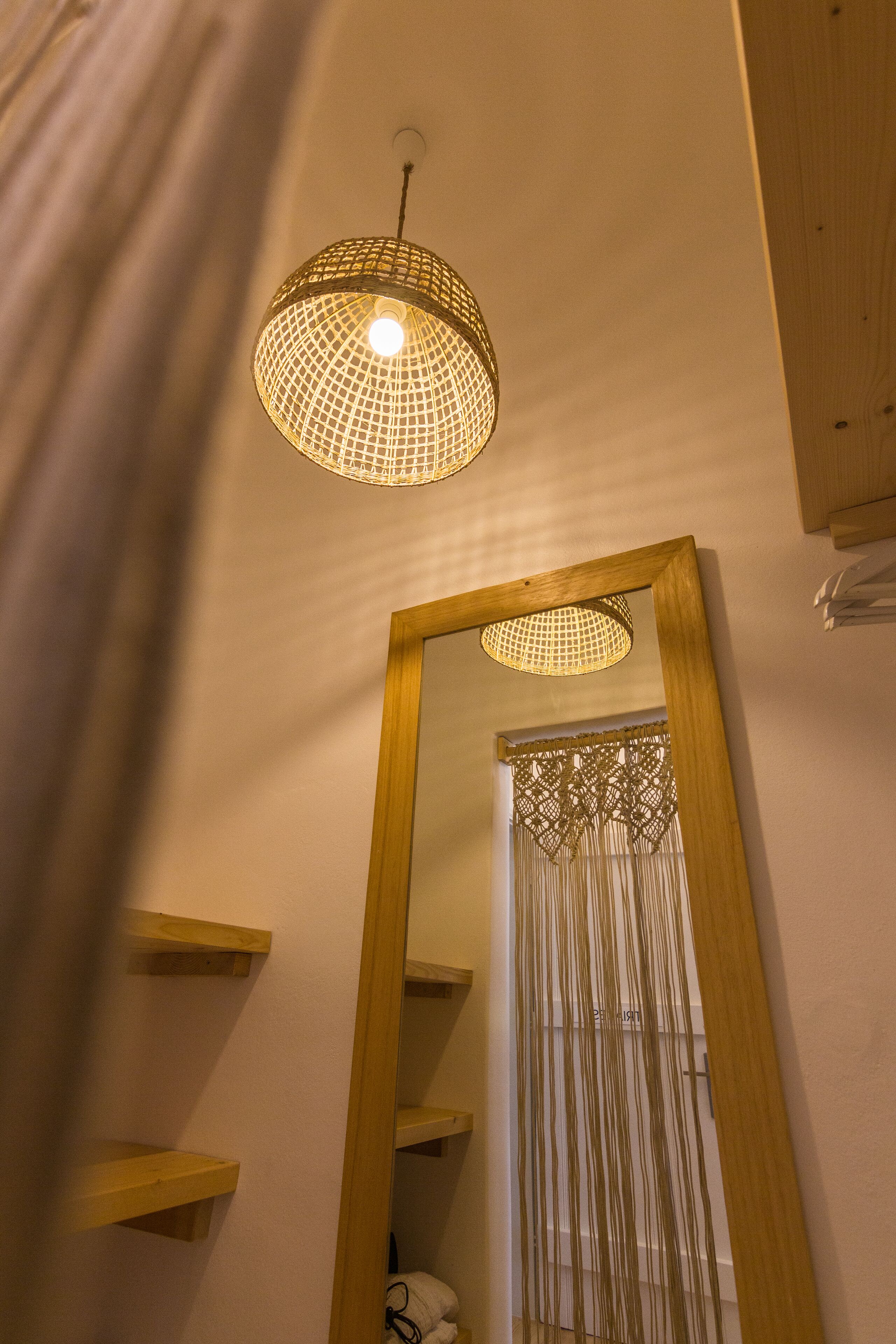 Una habitación con un espejo de marco de madera, una lámpara colgante y estanterías de madera.