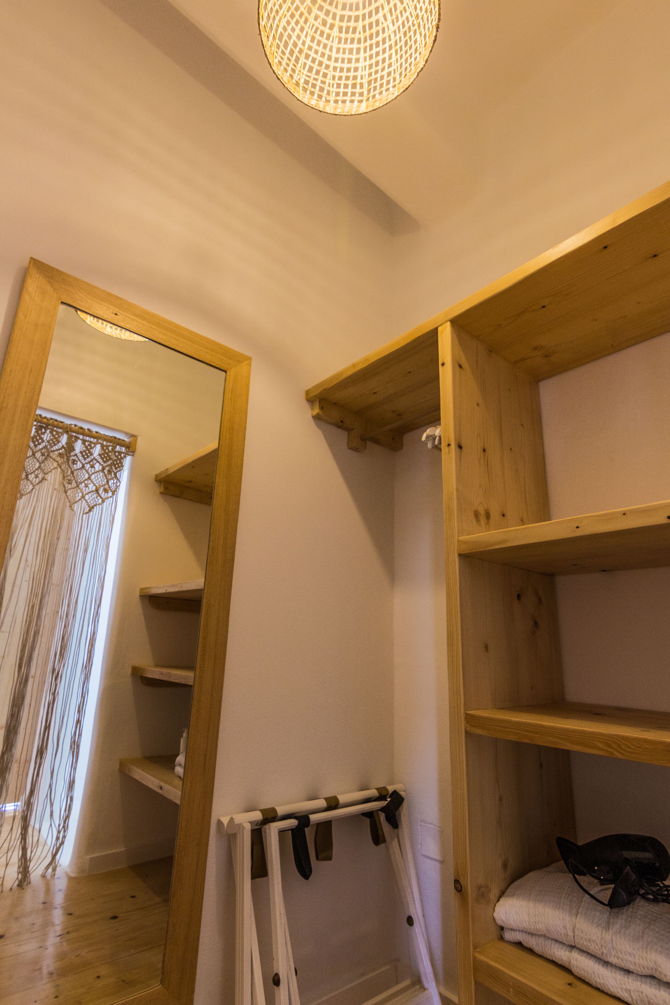 A wooden shelf unit with a mirror reflecting a lace door and a hanging rack.