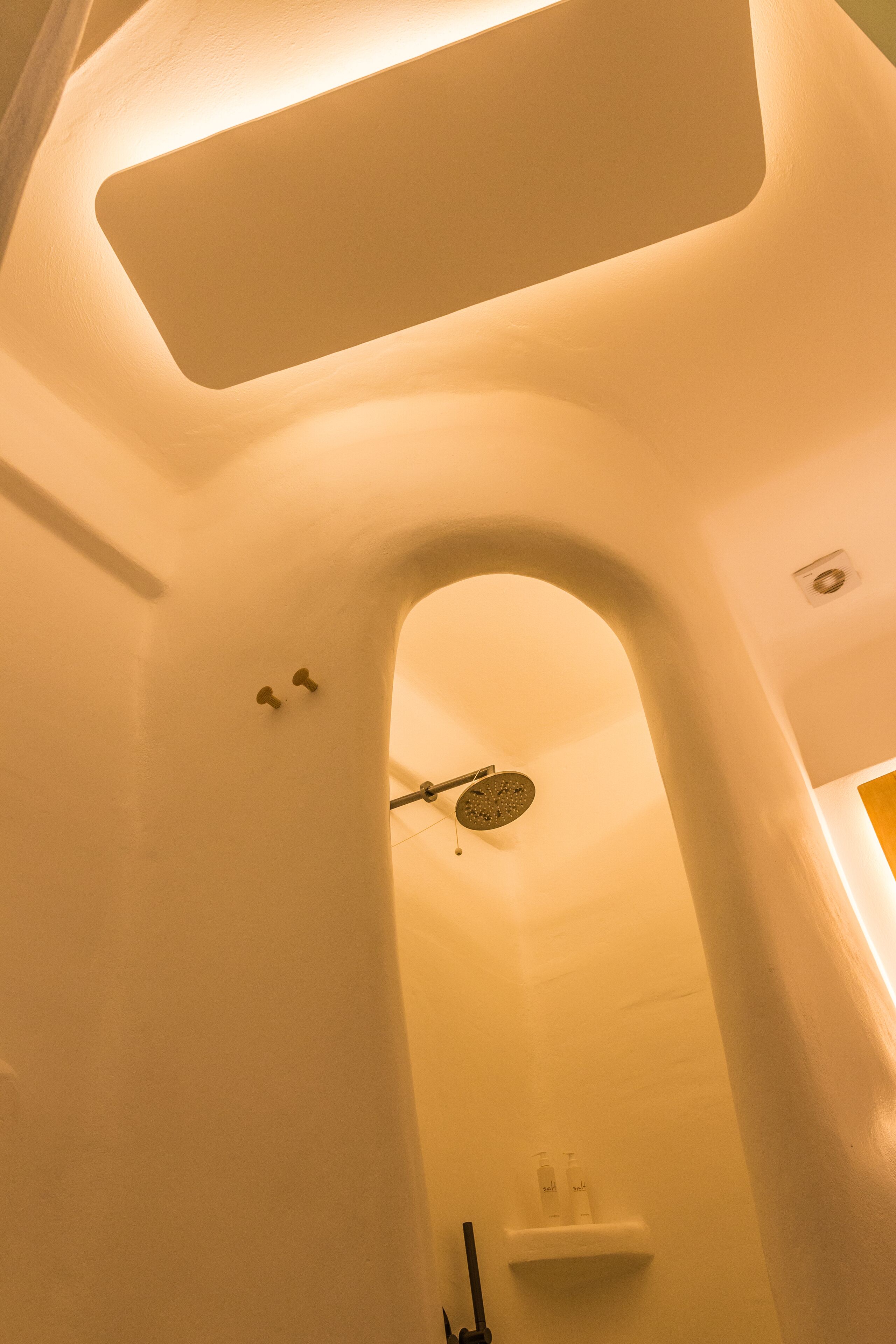 A bathroom with a shower, a towel rack, and a shelf with toiletries.