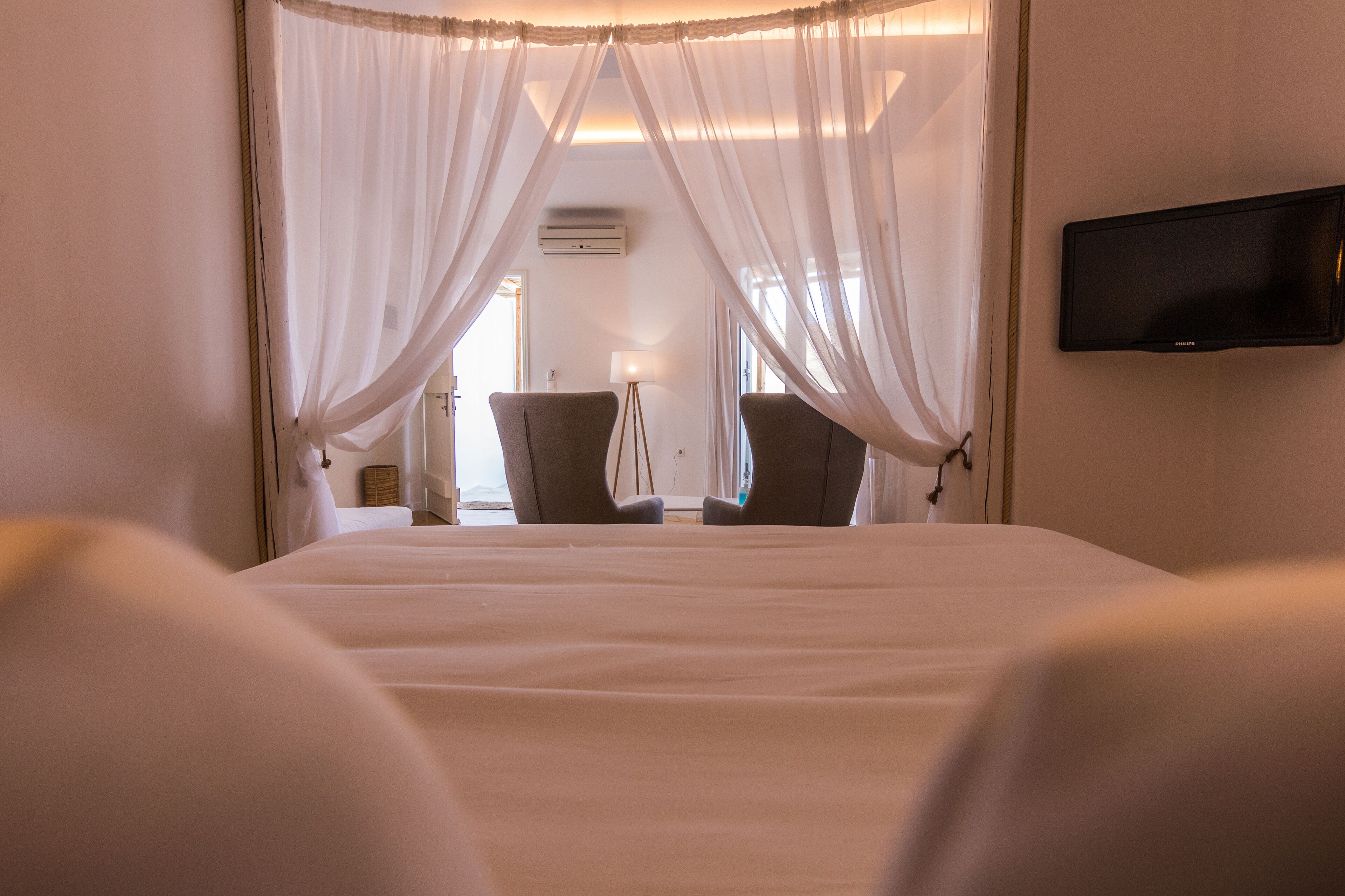 A hotel room with a bed, two chairs, a TV, and a lamp.