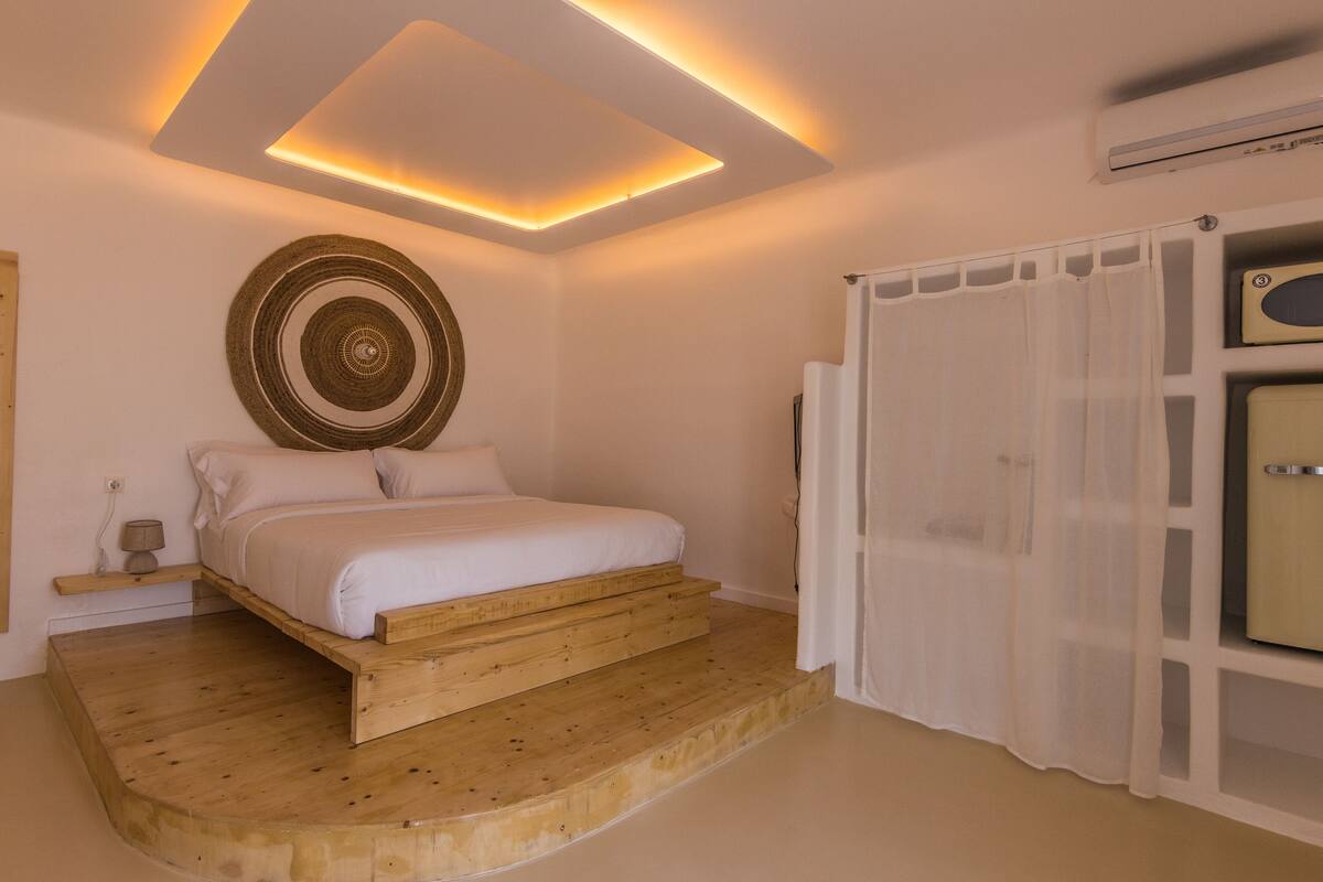 A bedroom with a bed on a wooden platform, a wall-mounted circular decoration, a white curtain, and a vintage radio.