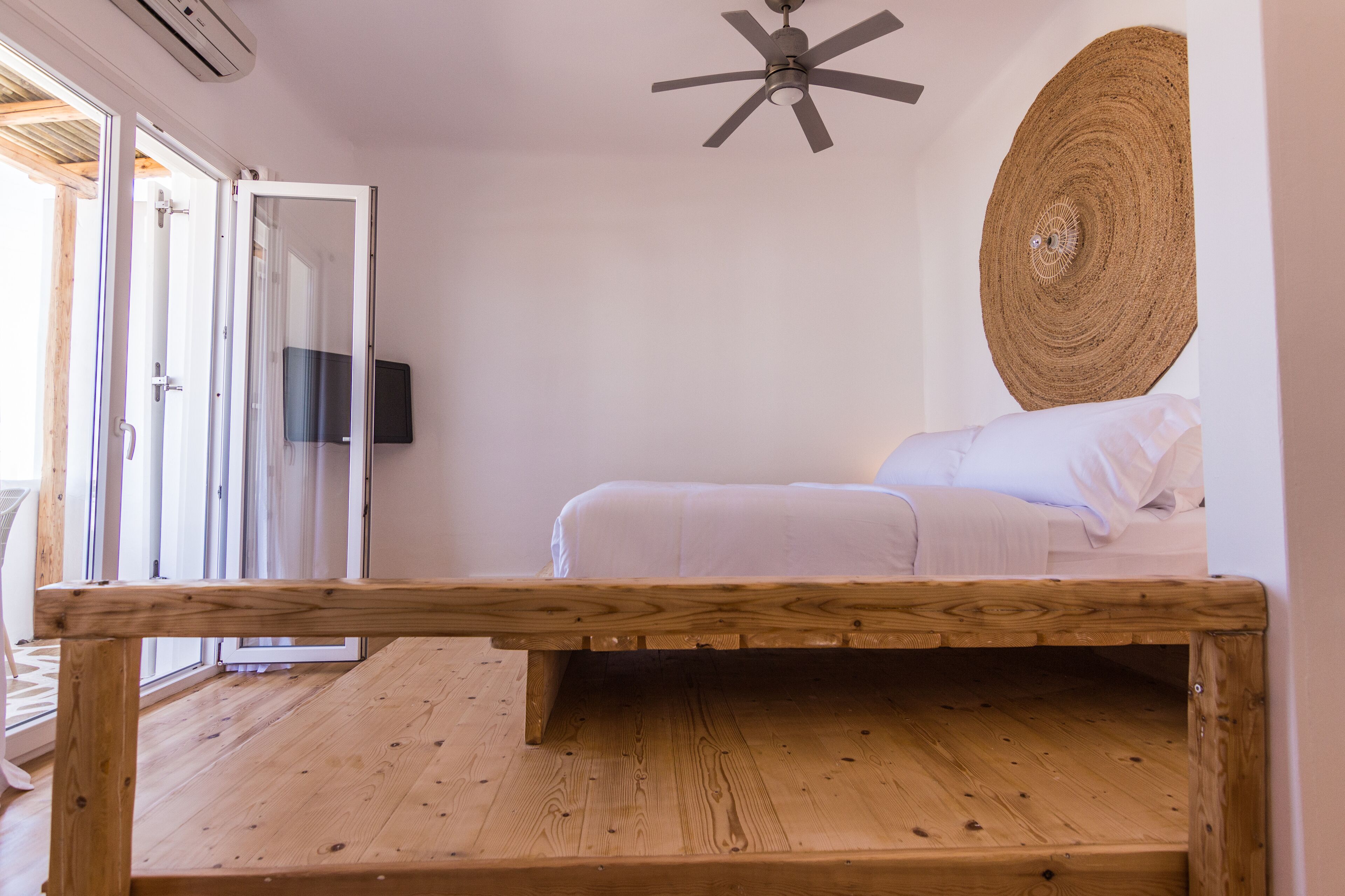 A bedroom with a bed, a ceiling fan, a woven wall hanging, and a wooden bench.