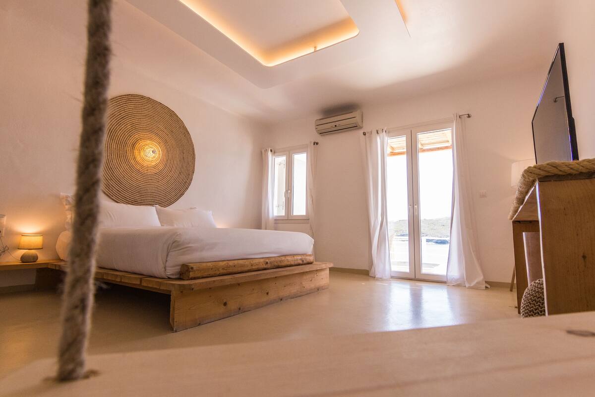 A bedroom with a wooden bed, a large circular wall decoration, and a view of the outdoors through the windows.