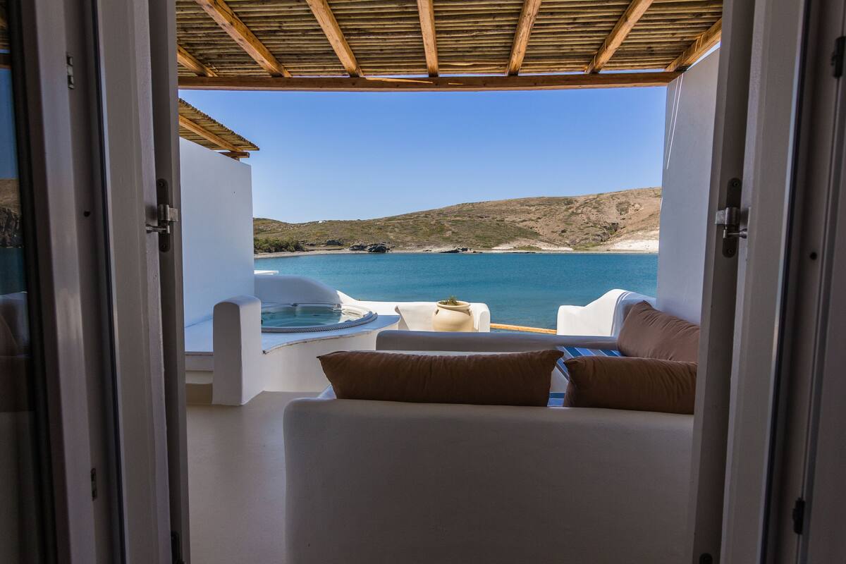 A balcony with a view of the sea and a white chair with a brown cushion.