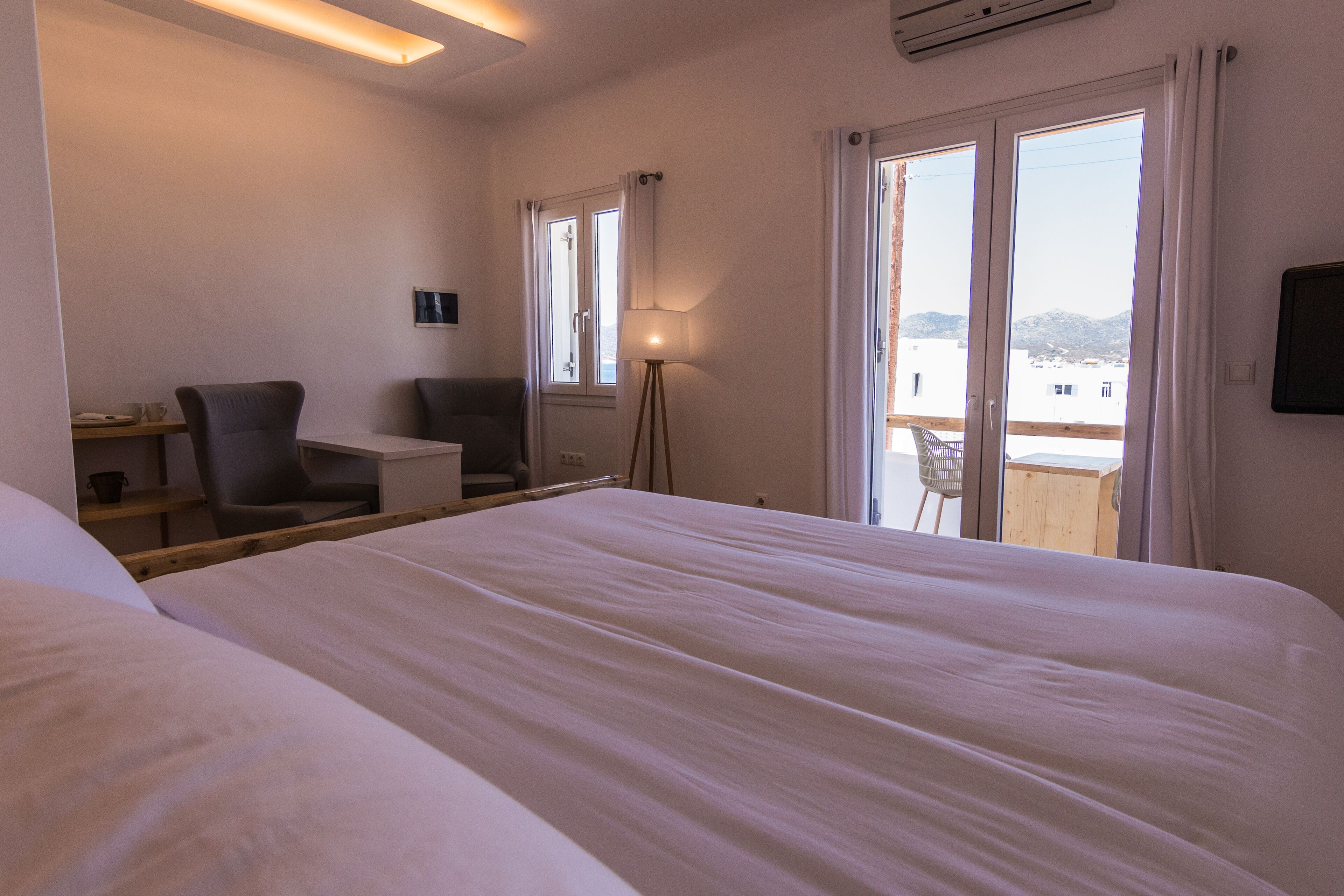 Habitación de hotel con una cama grande, un escritorio, una silla, una lámpara y un balcón con vistas.