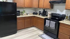 A kitchen with wooden cabinets, a black refrigerator, a stove, and a coffee maker.