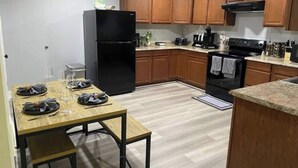 A modern kitchen with wooden cabinets, a black refrigerator, a dining table set with plates and glasses, and a microwave on the countertop.