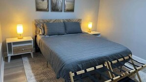 A bedroom with a bed, two bedside tables, a nightstand, a lamp, and a wall-mounted picture.