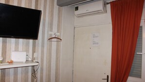 A room with a striped wall, a flat-screen TV mounted above a desk, an air conditioner, and a door with a red curtain. - Renovated Studio Olympiados (Thessaloniki)