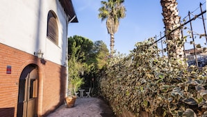A narrow cobblestone alley with a white building featuring a brick facade, a wooden door, and a small outdoor seating area with tables and chairs. - Euphorbia Apartment 2 in Catania by Wonderful Italy (Catania)