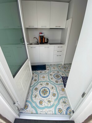 Una cocina compacta con armarios blancos, una cafetera y un suelo con diseño.
