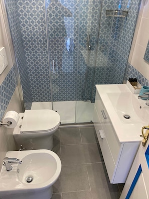 Un baño moderno con ducha envuelta en vidrio, inodoro, bidé y lavamanos.