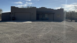 Ein Gebäude mit Garage, einer überdachten Terrasse mit Sitzgelegenheiten und einem Schotterweg.