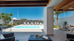 Zona junto a la piscina con sillones de descanso, una mesa con bebidas y vistas a la piscina y a las montañas.