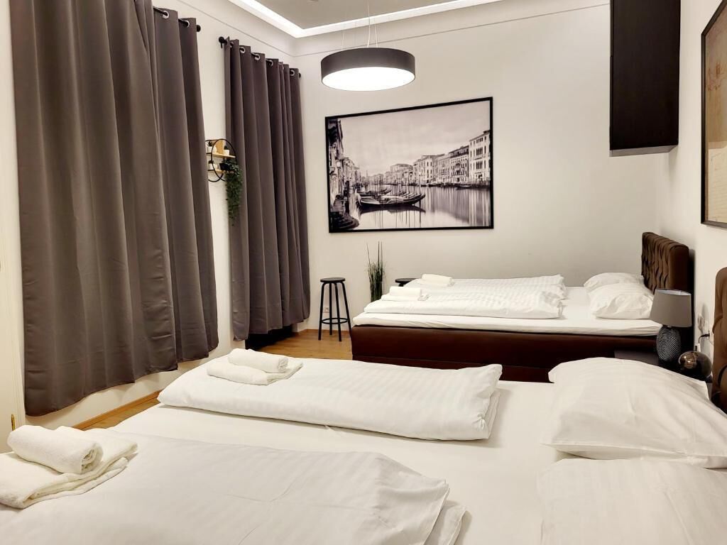 Ein Hotelzimmer mit zwei Betten, einem großen Fenster mit Vorhängen, einem gerahmten Bild an der Wand und einem Nachttisch mit Lampe.