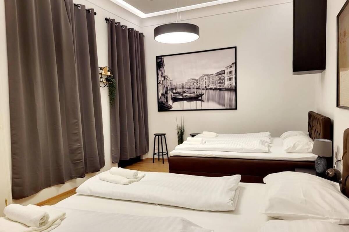 Ein Hotelzimmer mit zwei Betten, einem großen Fenster mit Vorhängen, einem gerahmten Bild an der Wand und einem Nachttisch mit Lampe.