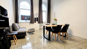 Ein modernes Wohnzimmer mit einem grauen Sofa, einem kleinen schwarzen Tisch und einem Essbereich mit einem Holztisch und schwarzen Stühlen.