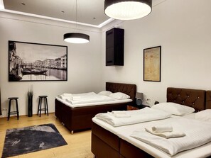 Une chambre d’hôtel moderne avec deux lits, un grand tableau représentant un paysage urbain, un meuble noir et un lampadaire noir.