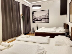 Une chambre d’hôtel avec deux lits, une grande fenêtre avec des rideaux, un tableau encadré au mur et une table de chevet avec une lampe.