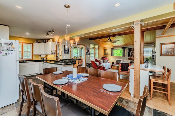 A spacious kitchen with white cabinets, a wooden dining table set for four, and a chandelier.