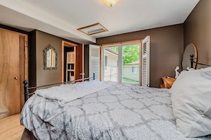 A bedroom with a bed, a wooden door, a mirror, and a window with shutters.