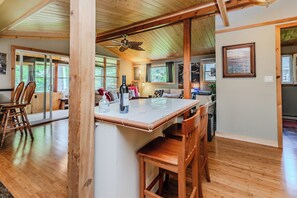 A spacious kitchen with a wooden ceiling, a central island with chairs, and a view of the adjacent living area.