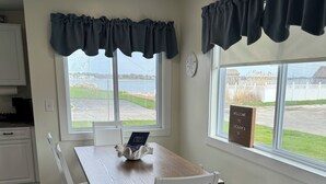 A dining area with a wooden table and white chairs, large windows with dark valance curtains, and a welcome sign by the window. - Quaint 1 Bed 1 bath private beach home. Long term renter welcome Dec 1 (Dartmouth)