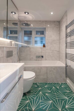 A modern bathroom with a bathtub, toilet, and a vanity with a mirror. - 2 Bedroom Apartment - 200m From Richmond Park (Kingston Upon Thames)