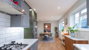A modern kitchen with a gas stove, cabinets, and a dining area with a table and chairs. - 2 Bedroom Apartment - 200m From Richmond Park (Kingston Upon Thames)