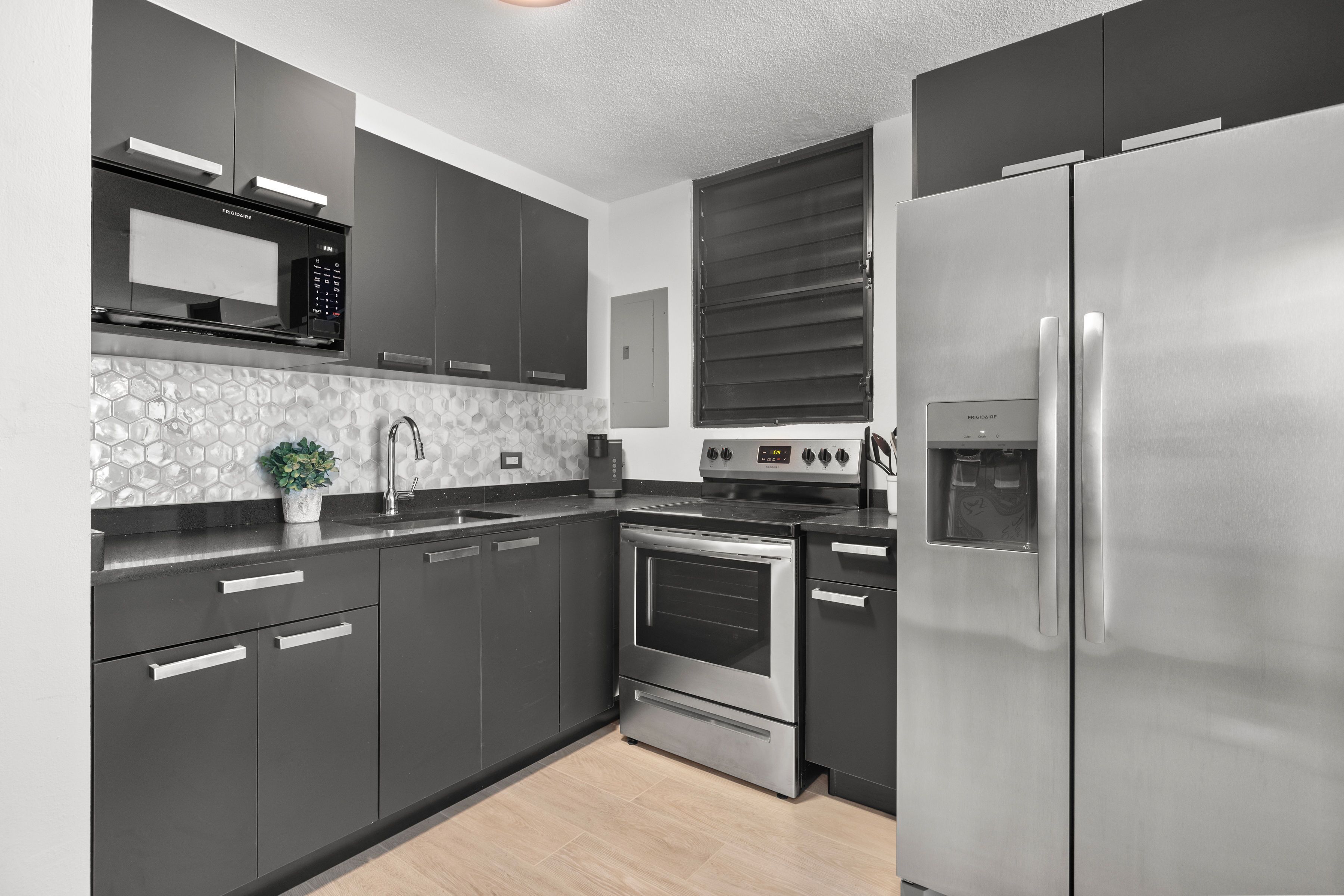 Una cocina moderna con armarios oscuros, un refrigerador de acero inoxidable, un horno empotrado y un microondas.