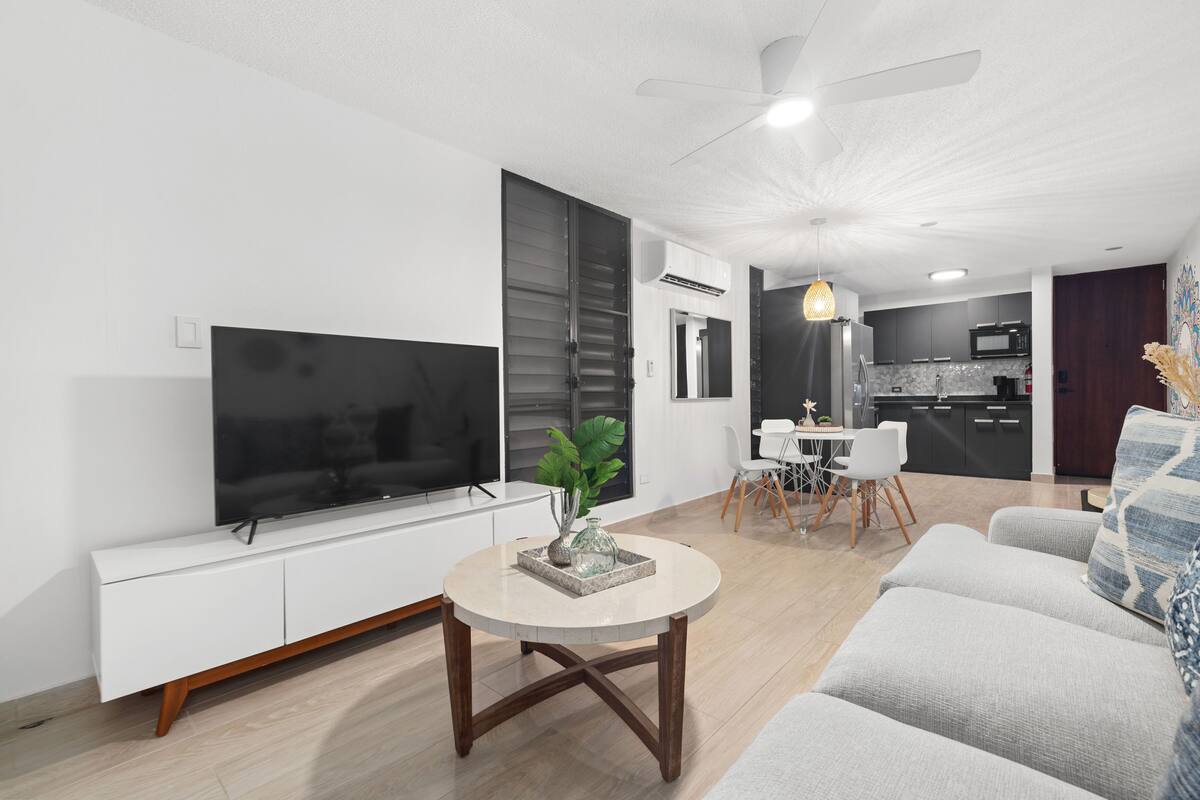 Una sala moderna con una televisión de pantalla plana, una mesa de centro redonda y un sofá.