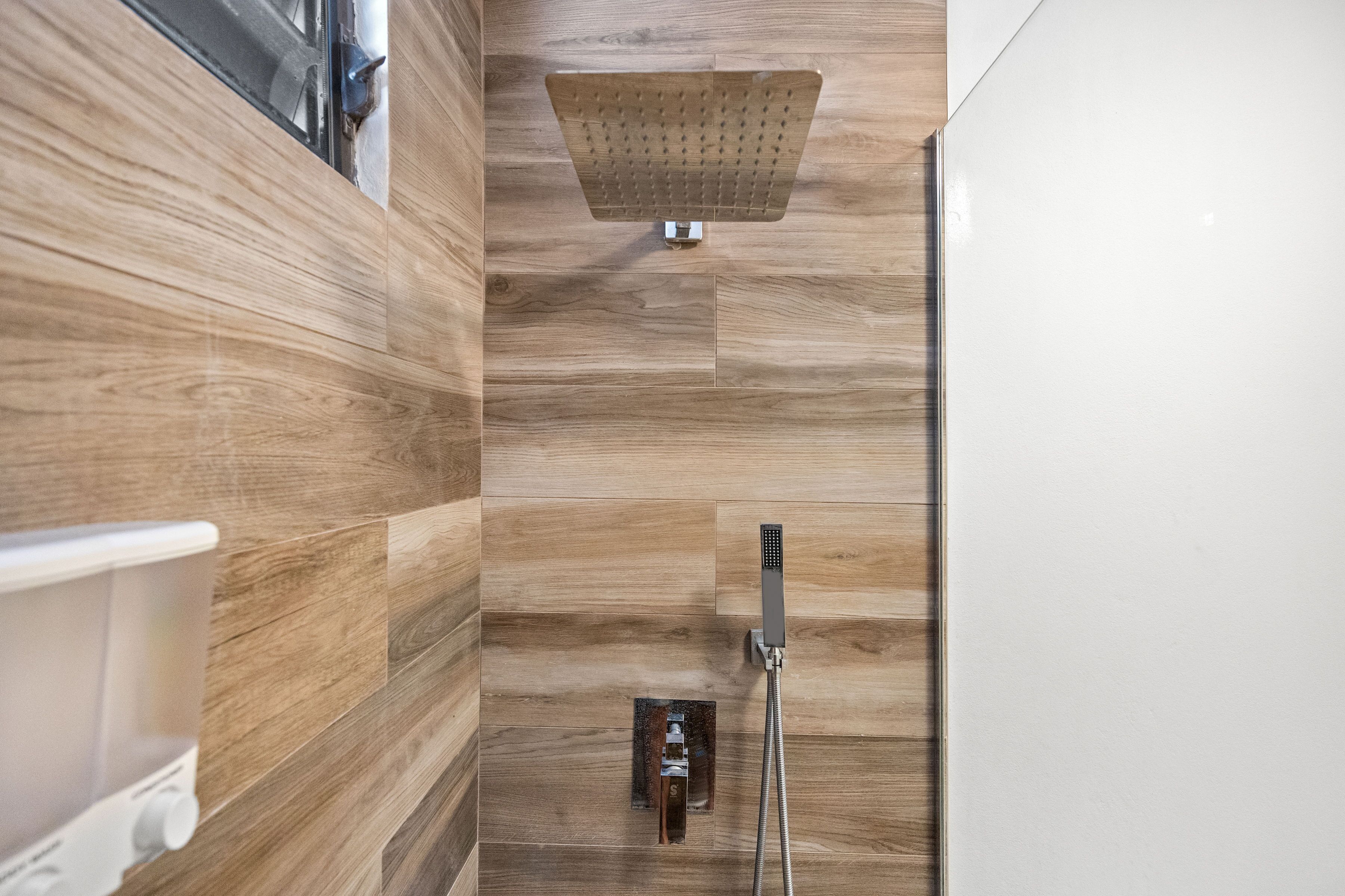 A modern bathroom with wooden paneling, a showerhead, and a handheld shower attachment.