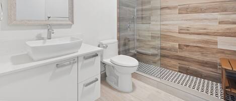 Un baño moderno con un espejo grande, un lavamanos, un inodoro y una zona de ducha con mampara de vidrio.