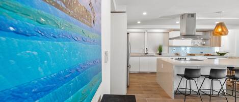 Une cuisine moderne dotée d’un grand îlot central, de tabourets de bar et d’un tableau accroché au mur.
