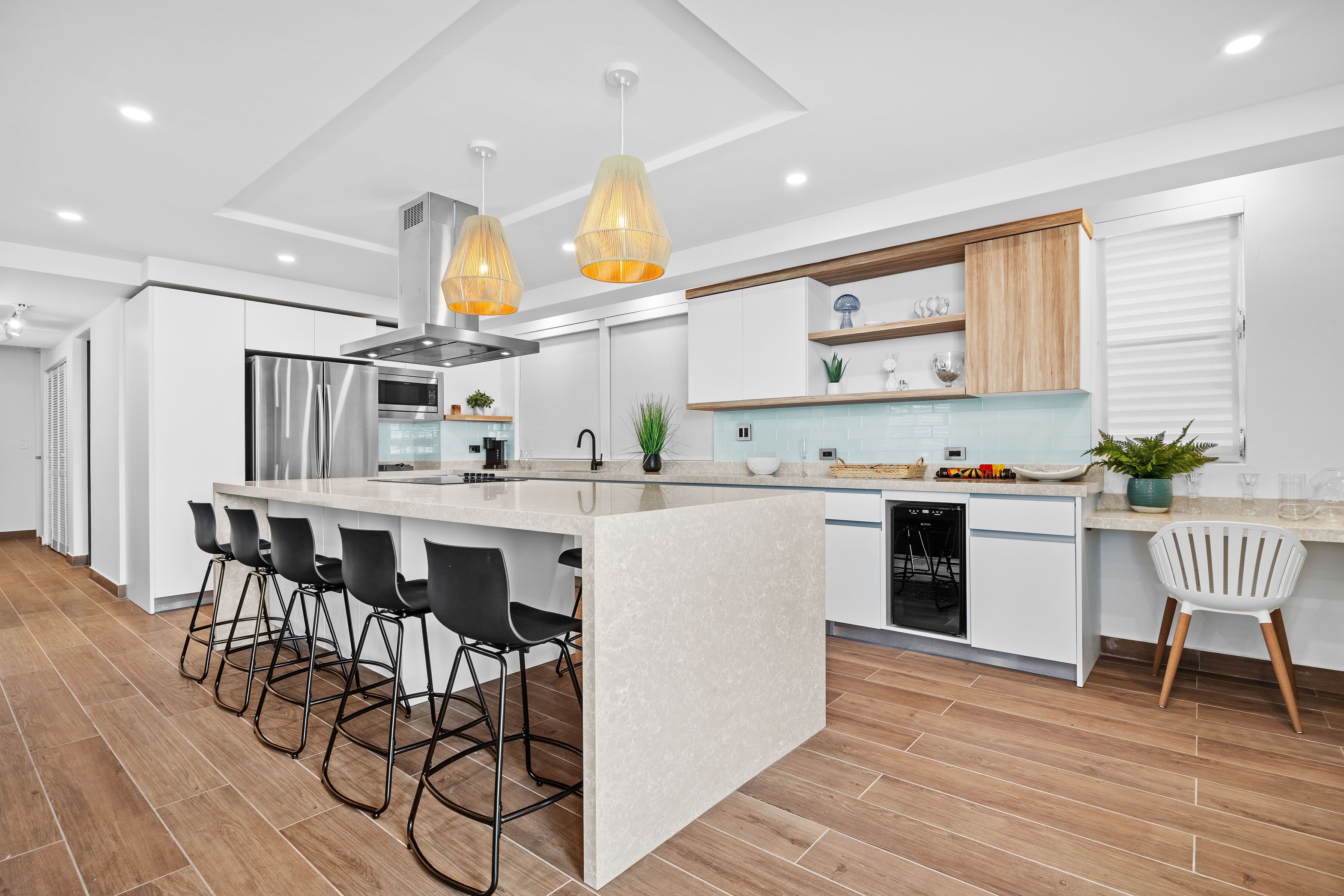 Una cocina moderna con una isla central, taburetes de bar, iluminación colgante y lavavajillas.