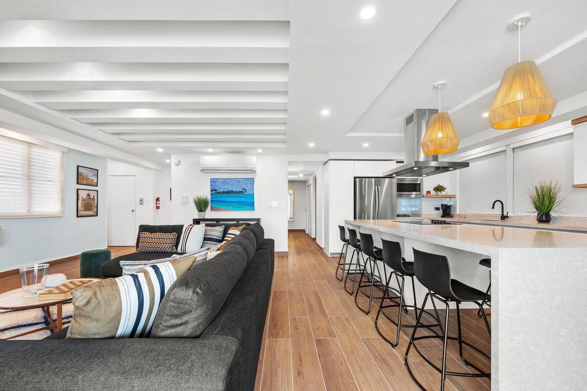 Una cocina moderna con una isla central, taburetes de bar e iluminación colgante.