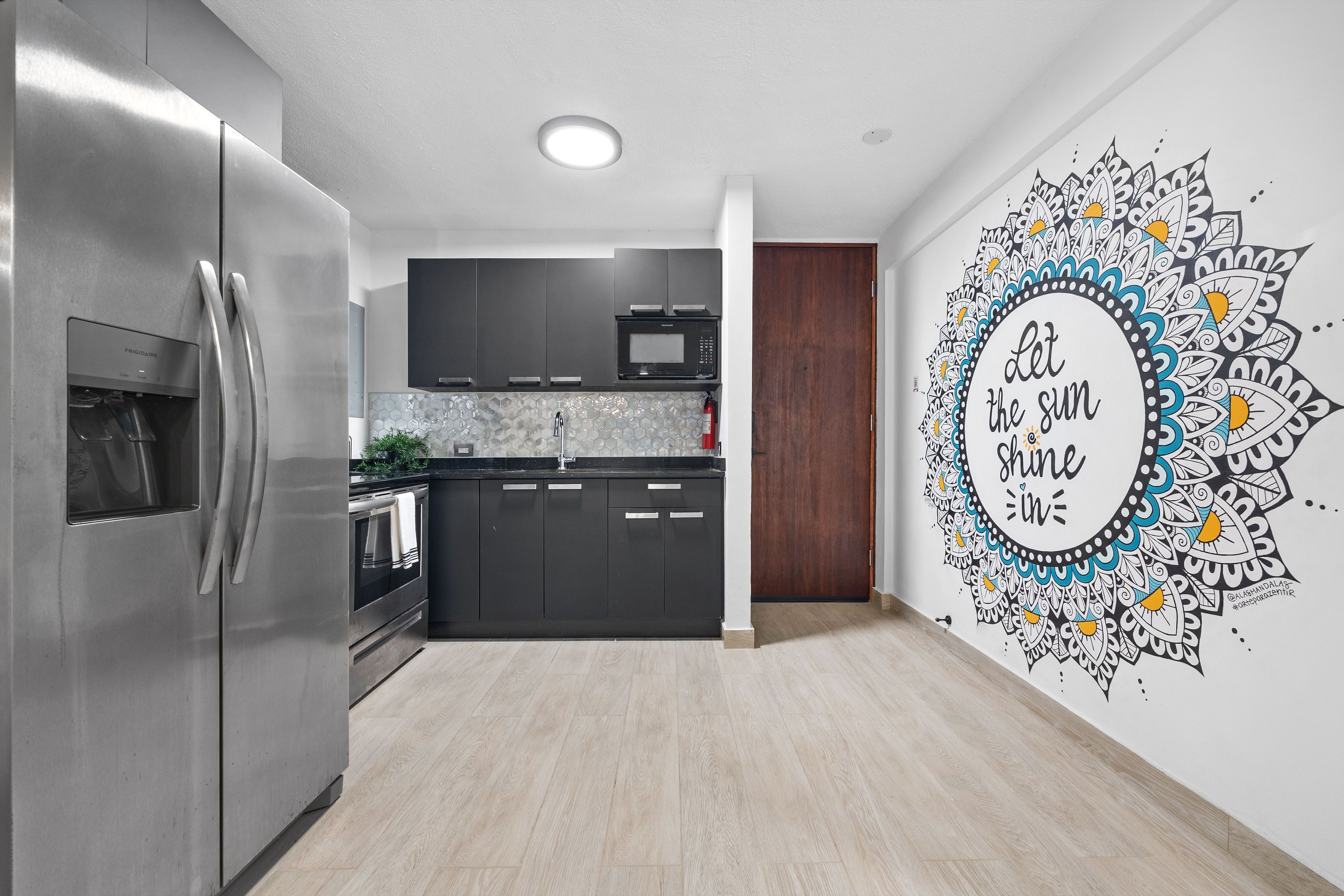 Une cuisine moderne dotée d’appareils électroménagers en acier inoxydable, de meubles de rangement aux couleurs sombres et d’une fresque murale décorative.