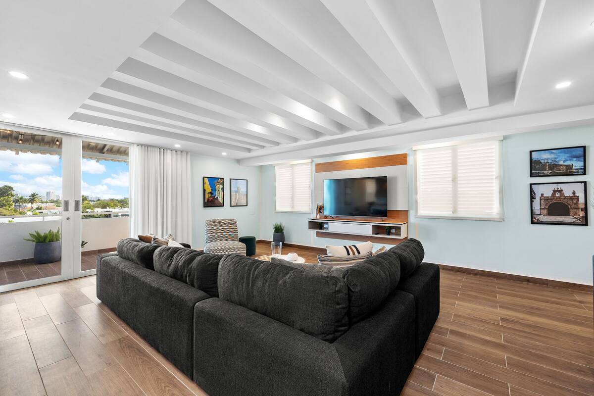 Una sala de estar moderna con un sofá seccional grande, un televisor de pantalla plana y un balcón con vistas a la ciudad.