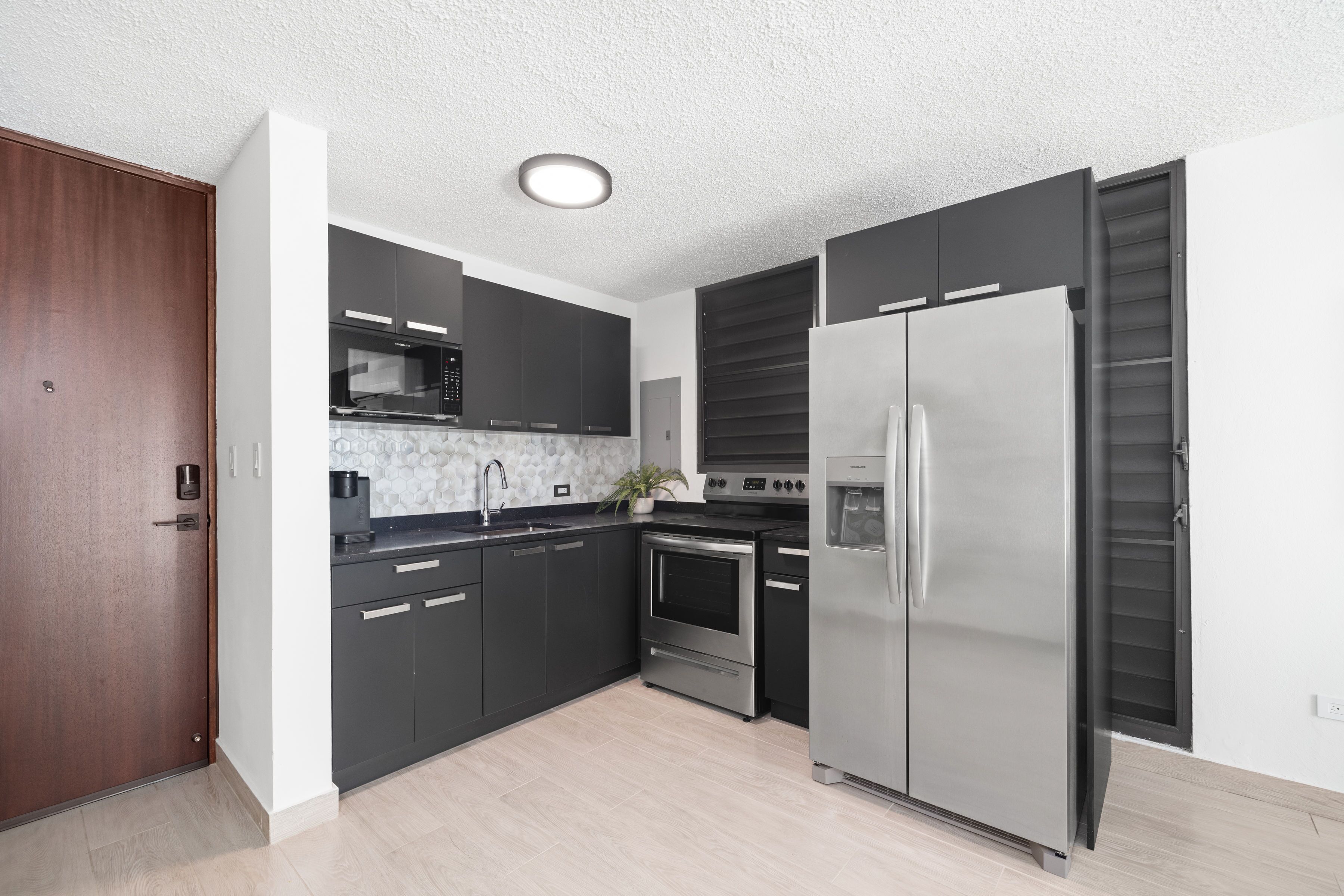 A modern kitchen with dark cabinets, stainless steel appliances, and a wooden door.
