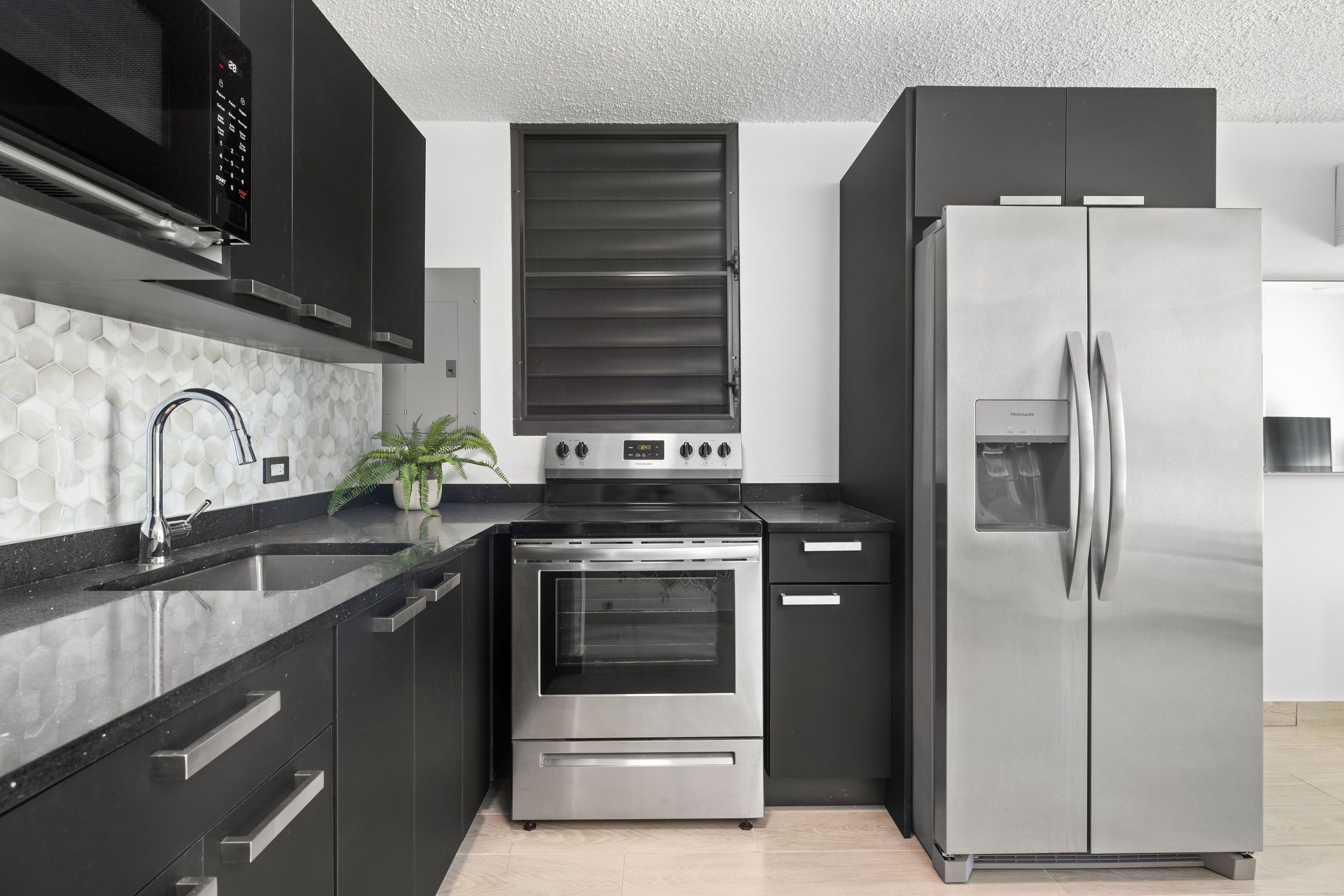 A modern kitchen with stainless steel appliances, black cabinetry, and a hexagonal tile backsplash.