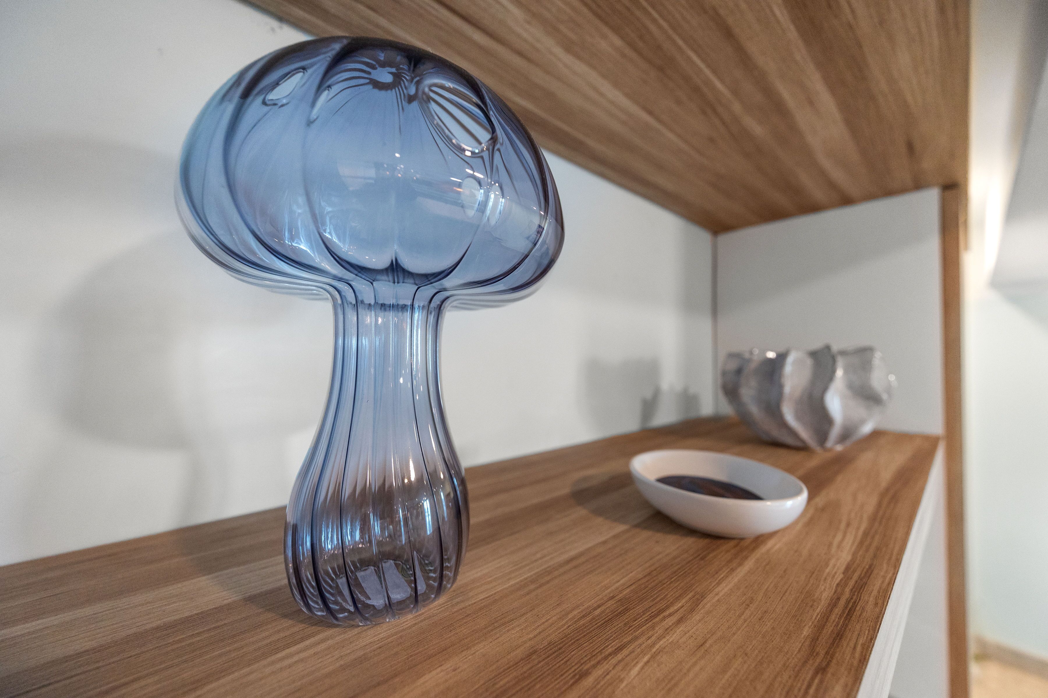 Een glazen vaas met helder water op een houten ondergrond, met een witte muur op de achtergrond.