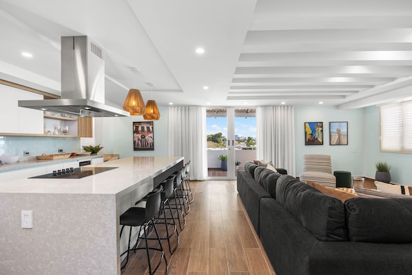 A modern kitchen with a central island, bar stools, and a large window.